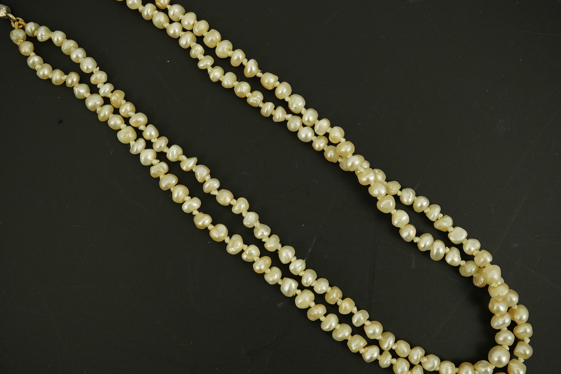 An antique twin strand baroque pearl necklace, with pearl set gold clasp bordered with single chain set with four graduated old mine cut diamonds